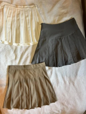 Tre plisserade kjolar i olika färger - Säljer tre snygga plisserade kortkjolar i vitt, grått och beige. Kjolarna har klassisk tennisstil med bred linning och veckad design.                                        Den VITA KJOLEN: XS                                                 Den GRÅA KJOLEN: S och den BRUNA KJOLEN M😊😊😊149kr/Styck