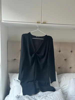 Svart långärmad klänning med v-ringning - Stilren svart klänning från Zara med lång ärm och djup v-ringning framtill. Klänningen har en lätt drapering vid bysten och är i en kort modell, perfekt för en trendig look.