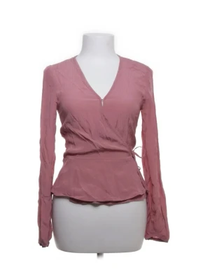 Rosa omlottblus med v-ringning - Trendig rosa omlottblus med v-ringning och långa ärmar. Blusen har en figurnära passform med knytband i sidan och lätt glansigt material som ger en snygg look. Perfekt att styla med jeans eller kjol för en chic outfit.