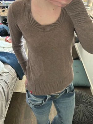 Brun stickad tröja med rund hals - Säljer en enkel och stilren brun stickad tröja med rundad halsringning och långa ärmar. Tröjan har ribbade muddar vid ärmslut och nederkant. Perfekt att matcha med jeans för en avslappnad look.