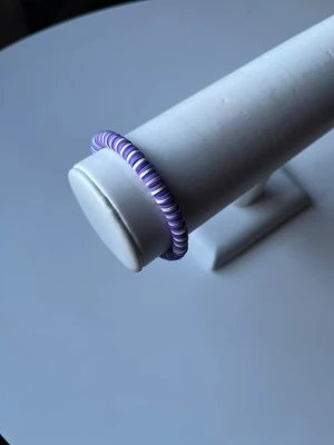 Lila och vitt armband -  Ett somrigt lila och vitt armband som har ett elastiskt band och även ett guldlås så man kan knäppa armbandet också. Armbandet är även handgjort.
