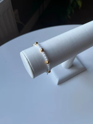 Vit och guldigt armband - Ett vit och guldit armband med elastiskt band så att det är lätt att ta på och av det är även handgjort.