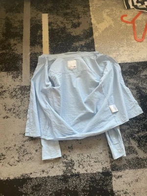 Ljusblå skjorta från 157 - Säljer en stilren ljusblå skjorta från 157. Skjortan har klassisk krage, långa ärmar och knappar framtill. Perfekt för dig som gillar enkel och clean stil. Tillverkad i mjuk bomull som känns skön mot huden.