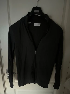 Mörkgrå full ziptröja från Selected Homme - Snygg mörkgrå full ziptröja från Selected Homme med hög krage och dragkedja framtill. Tröjan har en enkel och stilren design, perfekt att slänga på sig över en t-shirt. Långärmad och i mjukt material som känns skönt mot huden.