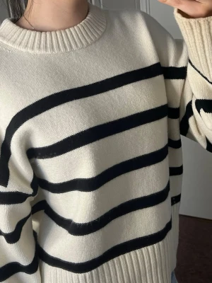 Vit stickad tröja med svarta ränder - Tröjan är beige/vit/offwhite med svarta ränder. Raka armar. 