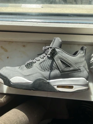 Gråa Air Jordan 4 sneakers - Säljer ett par gråa Air Jordan 4 sneakers med ovandel i mocka, meshpaneler på sidorna och vita samt svarta detaljer på sulan. Klassisk siluett med synlig Air-enhet i hälen och coola plastdetaljer vid snörningen.