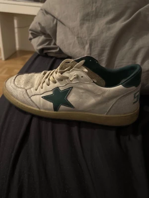 Vita Bape Sta sneakers med grön stjärna - Säljer ett par klassiska vita Bape Sta sneakers med grön stjärndetalj på sidan och grön häl. Skorna har perforerad tåbox, vita skosnören och en gulnad sula för retrovibe. Tillverkade i läder och har låg profil.