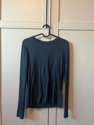 Mörkblå långärmad topp 157 - En enkel och stilren mörkblå långärmad topp från 157. Toppen har rund halsringning och är gjord i ett mjukt material som känns skönt mot huden. Perfekt att matcha med jeans eller kjol för en clean look.