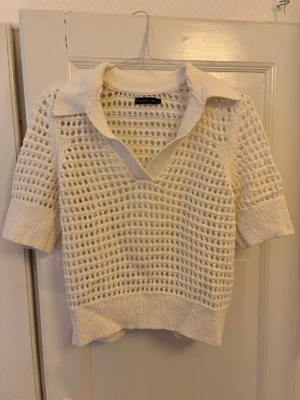 Vit stickad topp med krage - Snygg vit stickad topp från STOCKH LM med öppen hålstickning, bred krage och v-ringning. Tröjan har halvlånga ärmar och ribbade muddar vid ärmslut och nederkant. Perfekt för lager på lager och en cool, avslappnad stil. 
