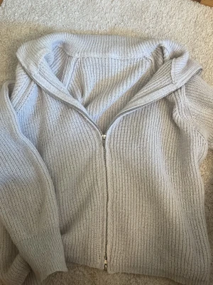 Kofta med dragkedja  - Mysig ljusgrå/beige stickad hoodie med dragkedja framtill. Tröjan har en avslappnad passform, ribbstickad struktur och huva. Perfekt för lager på lager och chill dagar. Materialet känns mjukt och stretchigt.