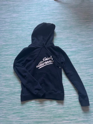 Svart Saint Laurent hoodie med tryck - Skön svart saint Laurent hoodie i storlek S. Osäker på äktahets för tagen är borta. Passar dig runt 175 cm. Skriv om det minsta lilla 😃