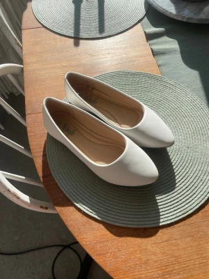 Vita ballerinaskor med spetsig tå - Säljer ett par stilrena vita ballerinaskor med spetsig tå och låg klack. Skorna har en enkel och modern design med slät ovandel i syntetmaterial och beige innersula. Perfekta för dig som gillar minimalistisk stil. Endast använda 1 gång