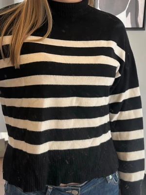 Svartvit randig stickad tröja - Säljer en svart stickad tröja med vita ränder ifrån ONLY. Tröjan har hög hals, långa ärmar och ribbstickade muddar. Tröjan har blivit lite nopprig men inget som syns. Pris kan diskuteras.