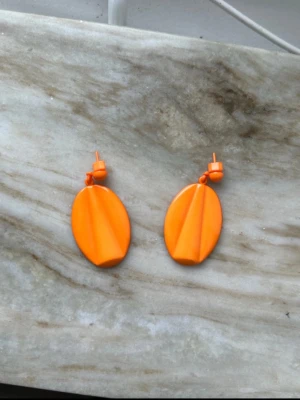 Orange vintage ovala örhängen 80-tal - Snygga örhängen i en stark orange färg med oval form och modern, stilren design. Tillverkade i plast med en matt finish och coola geometriska detaljer på framsidan. Perfekta för att ge din outfit en färgklick.