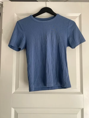 Mörkblå t-shirt i bomull - En enkel och stilren mörkblå t-shirt med rund hals och korta ärmar. Materialet känns mjukt och bekvämt, perfekt för en chill look. Passformen är normal och t-shirten har en klassisk design utan mönster eller extra detaljer.