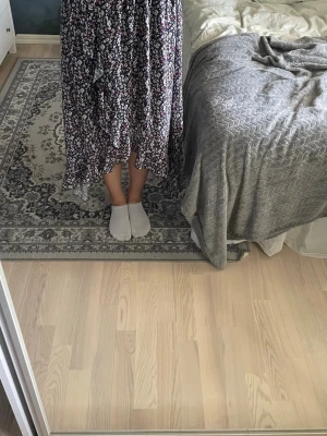 Blommig långkjol i lila  - Säljer en flowy långkjol med blommigt mönster i lila, vitt och inslag av rött. Kjolen har en avslappnad passform och är perfekt för dig som gillar en bohemisk stil. Materialet känns lätt och skönt, troligtvis polyester eller bomull.