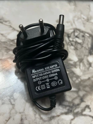 Svart adapter/datorladdare 12V 2A - Säljer en svart nätadapter från KM-SHENG med 12V DC och 2000mA utgång. Passar till olika elektronikprylar och har en klassisk rund kontakt. Tillverkad i plast och har tvåpolig kontakt för vägguttag. Perfekt även för datorladdare 
