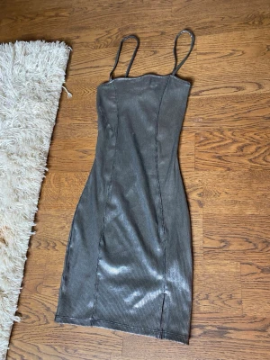 Glittrig silver klänning med smala band - Säljer en snygg glittrig silverfärgad klänning med smala axelband och figurnära passform. Klänningen har en lätt skimrande yta och är gjord i ett stretchigt material som sitter tajt. Perfekt för dig som vill sticka ut lite extra.