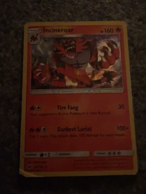 Pokémonkort Incineroar - Säljer ett Pokémonkort med Incineroar-motiv. Kortet har en röd och gul ram, och visar Incineroar i en kraftfull pose. Texten är på engelska och kortet har attacker som Fire Fang och Darkest Lariat. Perfekt för samlare eller Pokémonfans.