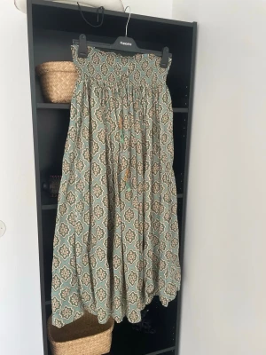 Mönstrad långkjol från Zara - Säljer en flowy långkjol från Zara  med grönt och beige orientaliskt mönster. Kjolen har resår i midjan och ett luftigt fall, perfekt för varma dagar. Säljs inte längre.