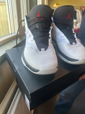 Nike Air Jordan vita sneakers - Snygga vita Nike Air Jordan sneakers med svart plös och röda detaljer. Klassisk Jordan-logga på plösen och slitstark sula med Nike Air-märkning undertill. Ovandelen är i skinn och textil, med snörning framtill för perfekt passform.