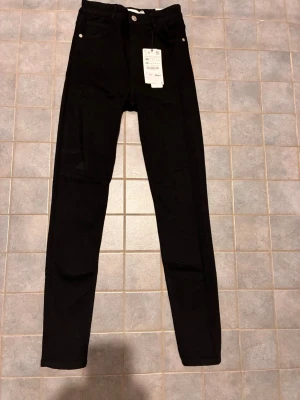 Svarta skinny jeans från Zara  - Svarta skinny jeans från Zara  med klassisk femficksdesign och hög midja. Jeansen har smal passform och stretchigt material som sitter snyggt. Perfekta till en cool och stilren look. Nytt skick med kvitto.