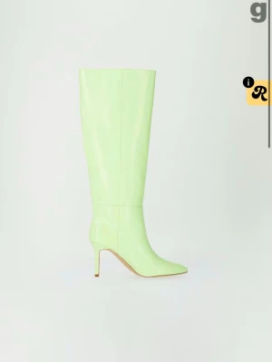 Ljusgröna höga boots med klack - Säljer ett par ljusgröna knähöga boots med spetsig tå och smal klack. Stövlarna har en glansig finish och ett croco-mönstrat konstläder som ger en trendig look. Perfekta för dig som vill sticka ut med färg och stil.