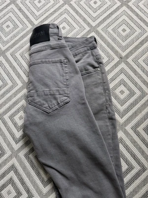 Gråa slim fit jeans från Calvin Klein - Snygga gråa slim fit jeans från Calvin Klein med klassisk femficksmodell och svart patch med logga bak i midjan. Jeansen har normalhög midja och raka ben. Tillverkade i mjukt bomullsmaterial med lite stretch för extra komfort.