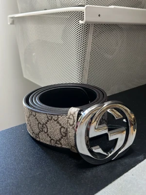 Gucci GG beige bälte med silverdetalj - Snyggt beige bälte från Gucci med klassiskt GG-mönster och stor silverfärgad logga som spänne. Bältet har en stilren design och passar perfekt till jeans eller byxor för att lyfta din outfit. A kopia 115 cc 