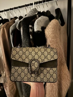 Gucci Dionysus GG axelväska beige - Säljer en Gucci Dionysus axelväska i beige canvas med klassiskt GG-mönster och detaljer i mocka. Väskan har en snygg silverfärgad kedjerem och ett statement-spänne framtill. 