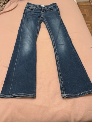 Blå bootcut jeans från Gina Tricot - Snygga blå bootcut jeans från Gina Tricot med klassisk femficksdesign och markerade sömmar. Jeansen har lätt slitna detaljer framtill och vida ben. Perfekta för dig som gillar en trendig stil.