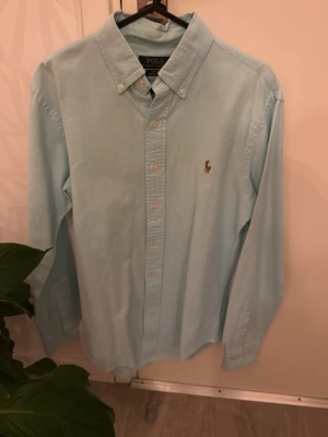 Ljusblå skjorta från Ralp lauren ny skick - Säljer en stilren ljusblå skjorta från Polo Ralph Lauren med klassisk button-down krage och broderad logga på bröstet. Skjortan är i slim fit och tillverkad i bomull med stretch för extra komfort. Perfekt till jeans eller chinos!