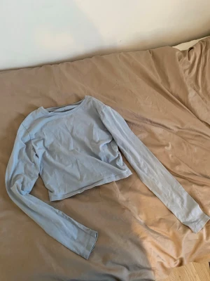 Ljusblå croppad långärmad topp -  ljusblå kort  topp med långa ärmar och rund halsringning. Perfekt att matcha med höga jeans eller kjol för en avslappnad och snygg look.  