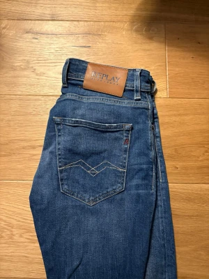 Blå jeans från Replay med raka ben - Snygga blå jeans från Replay med klassisk femficksdesign och raka ben. Jeansen har knäppning med knappar och detaljerade sömmar på bakfickan. Märkespatch i läder baktill i midjan. Perfekta för en avslappnad och trendig look.