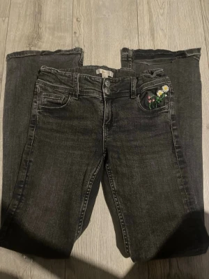 Svarta jeans med broderade blommor - Dessa jeans hade varit på läger pris men de har broderade blommor på en främre ficka som en brksnt har gjort till mig! de passar tyvärr inte längre dock. Snygga svarta jeans med broderade blommor i färg på fickan. Jeansen har klassisk femficksmodell, raka ben och rå kant nedtill för en trendig look. Perfekta för dig som vill ha något unikt i garderoben.