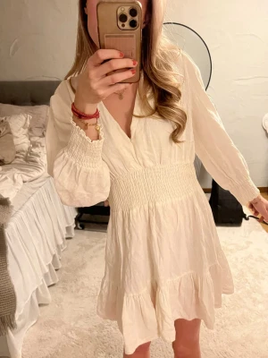 Vit Zara klänning  - Söt vit klänning från Zara. Den har långa ärmar och har en bred resor i midja samt vid ärmarnas slut. Kjolen har volangkant och klänningen är gjord i ett lätt, luftigt tyg perfekt nu till sommaren. Om du har frågor, tveka inte att höra av dig!💕💕