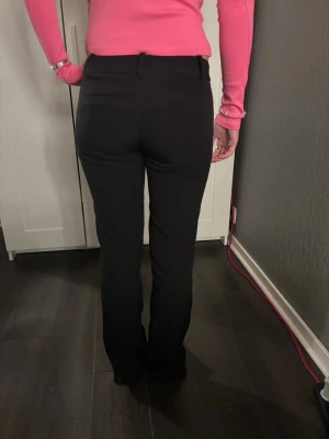 Svarta bootcut kostymbyxor - Säljer ett par svarta kostymbyxor med bootcut passform och låg midja i strl 36. Dem är lite slitna längst ner på benen som man kan se på sista bilden. Byxorna har bälteshällor, diskreta bakfickor och stängs med dragkedja och knapp. Perfekta till en snygg topp eller skjorta. Materialet är mjukt.