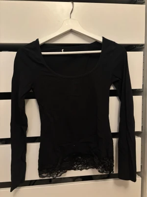 Svart långärmad topp med spetskant - Snygg svart långärmad topp med bred urringning och dekorativ spetskant nedtill.