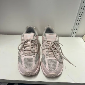 New Balance rosa sneakers 39 - Säljer ett par ljusrosa New Balance sneakers med meshpaneler och detaljer i grått. Skorna har en chunky sula och klassisk logga på sidan. Perfekta för dig som gillar sportig och trendig stil.
