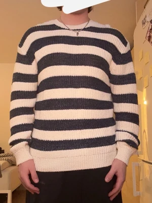Randig stickad tröja i blått och vitt - Säljer en stickad tröja med breda horisontella ränder i marinblått och vitt. Tröjan har rund halsringning, långa ärmar och ribbade muddar vid ärmslut och nederkant. Perfekt för dig som gillar klassisk och avslappnad stil.