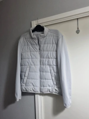 Ljusgrå pufferjacka från Zara - Snygg ljusgrå pufferjacka från Zara med ståkrage och dragkedja framtill. Jackan har två snedställda fickor och quiltad design på framsidan. Perfekt för kalla dagar och enkel att matcha med olika outfits.