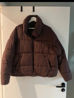 Brun pufferjacka från Bik Bok - Säljer en brun pufferjacka från Bik Bok i storlek L. Jackan har hög krage, dragkedja framtill och två fickor. Tillverkad av återvunnet material och har en boxig, trendig passform som håller dig varm under kalla dagar. Finns på fler sidor