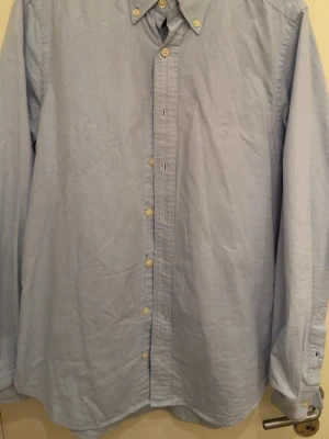 Ljusblå skjorta från Gant - Klassisk ljusblå skjorta från Gant med button-down krage och vita knappar. Skjortan har lång ärm och diskret broderad logga på bröstet. Tillverkad i mjuk bomull för en bekväm känsla och stilren look.