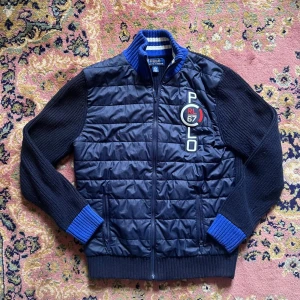 Sjukt snygg cardigan från Polo Ralph Lauren 14-16 (passar XS) - Snygg blå quiltad jacka från Polo Ralph Lauren med stickade ärmar och krage i blått och vitt. Jackan har dragkedja framtill, två fickor och en stor Polo RL67-logga på bröstet. Perfekt för dig som gillar sportig och stilren look.