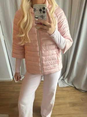 Ljusrosa dunjacka med trekvartsärm - Snygg ljusrosa dunjacka med trekvartsärmar och dragkedja framtill. Jackan har quiltad design och kortare ärm. I nyskick! Står att jackan är L men mycket liten i storlek så mer S. 