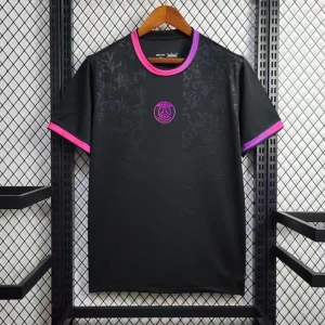 Svart PSG t-shirt med rosa detaljer - Snygg svart t-shirt från PSG med diskret mönster framtill och klubbens logga i rosa på bröstet. T-shirten har korta ärmar och kontrasterande rosa kant vid hals och ärmslut. Perfekt för dig som gillar sportig stil och vill sticka ut lite extra. 