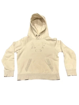 Abercrombie & Fitch hoodie vintage créme/off white - Plagget har worn/vintage look med naturligt slitage som ger karaktär. Lätt fransning vid sömmar och runt huvan, inget som påverkar användning, endast estetiskt. Se bilder.                    • Skick: used / vintage                                                  • Passform: classic fit                                                  • Original metalldetaljer                                        Skriv vid frågor eller fler bilder 🤝 