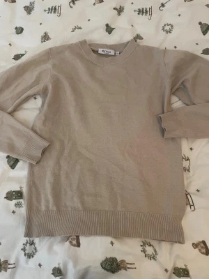 Beige stickad tröja från RYVLS - En stilren beige stickad tröja från RYVLS Stockholm. Tröjan har rund halsringning, långa ärmar och ribbade muddar vid ärmslut och nederkant. Perfekt för lager på lager och enkel att matcha med olika outfits.