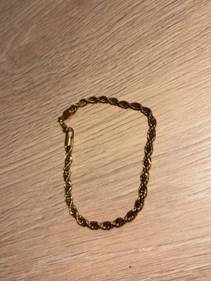Guldtonat tvinnat armband - Snyggt armband i guldfärgad metall med tvinnad kedja och enkel karbinhake. Armbandet har en klassisk och stilren design som passar till många olika looks. Perfekt accessoar för dig som gillar guldsmycken och vill ha något som sticker ut lite extra.