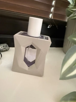 Ariana Grande God is a woman - Säljer en Ariana Grande parfym i en unik, geometrisk lila glasflaska med vit plastkork. Flaskan har ett coolt, modernt hölje i matt ljusgrått och parfymen syns genom ett fönster i mitten. Perfekt för dig som gillar snygg design och fräscha dofter. Lådan finns ej kvar och endast testad.